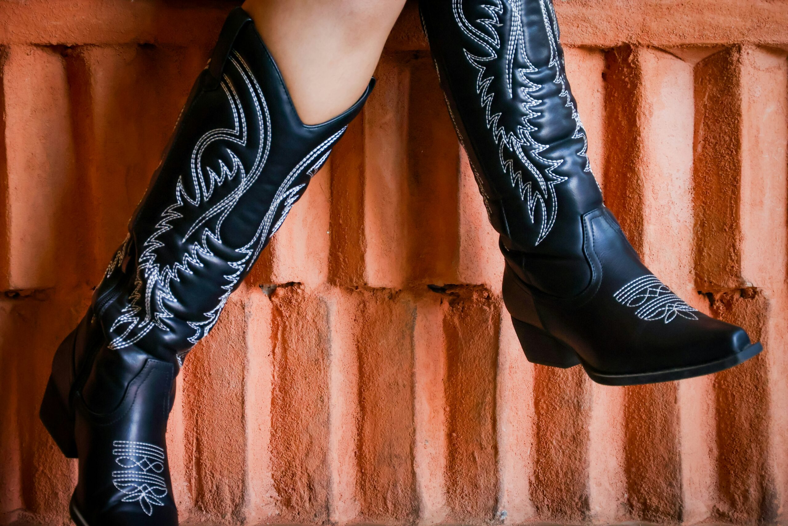 Black embroidered cowboy boots on a brick background, modern western style
